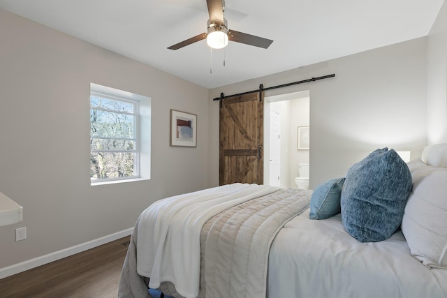 bedroom with ceiling fan, ensuite bath, a barn door, and dark wood-type flooring