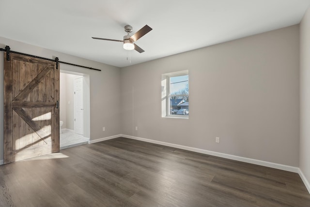 spare room featuring dark wood-type flooring, a barn door, and ceiling fan