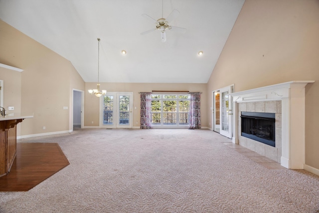 unfurnished living room featuring ceiling fan with notable chandelier, light colored carpet, a fireplace, and high vaulted ceiling