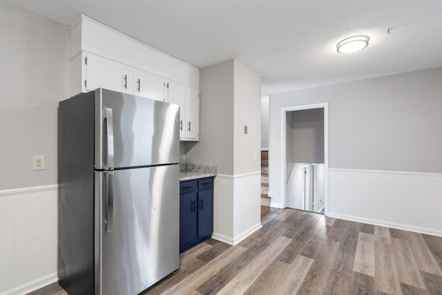 kitchen featuring blue cabinetry, a textured ceiling, wood-type flooring, white cabinetry, and stainless steel fridge