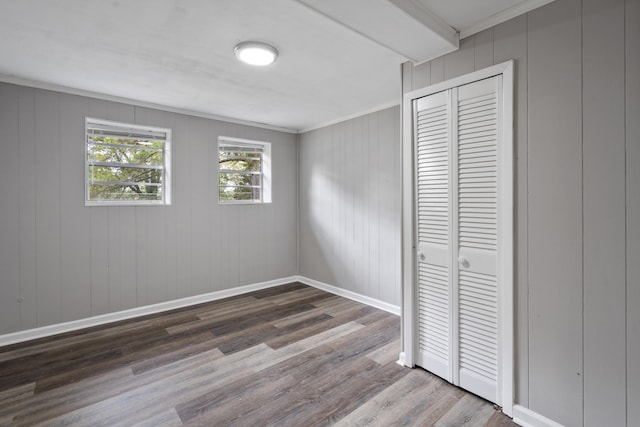 unfurnished bedroom featuring crown molding, wood-type flooring, wooden walls, and a closet