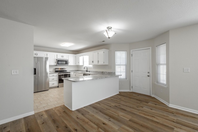 kitchen featuring sink, white cabinetry, stainless steel appliances, wood-type flooring, and kitchen peninsula