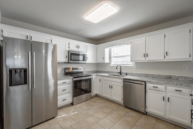 kitchen featuring appliances with stainless steel finishes, sink, white cabinets, light tile patterned floors, and light stone counters