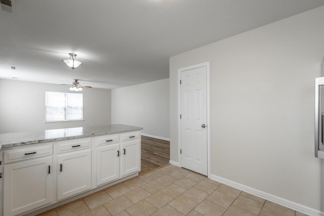 kitchen with light tile patterned floors, light stone countertops, white cabinets, and ceiling fan