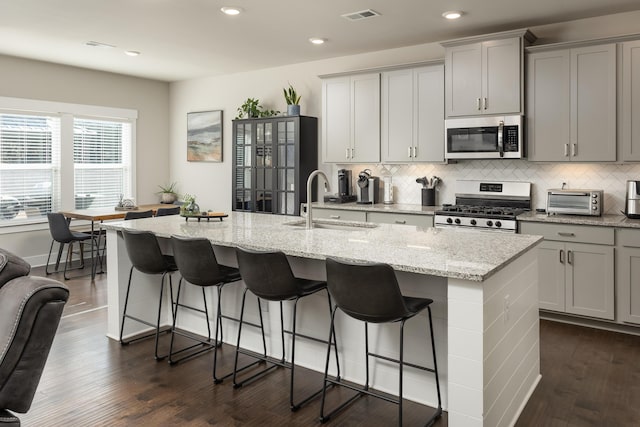 kitchen with sink, stainless steel appliances, a kitchen island with sink, and a kitchen bar