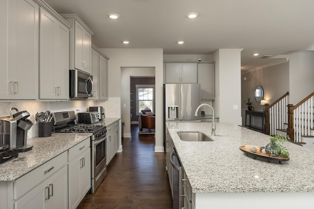 kitchen featuring sink, an island with sink, light stone counters, and appliances with stainless steel finishes