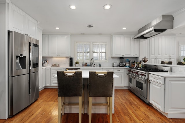 kitchen with a kitchen island, appliances with stainless steel finishes, white cabinets, a kitchen bar, and wall chimney exhaust hood