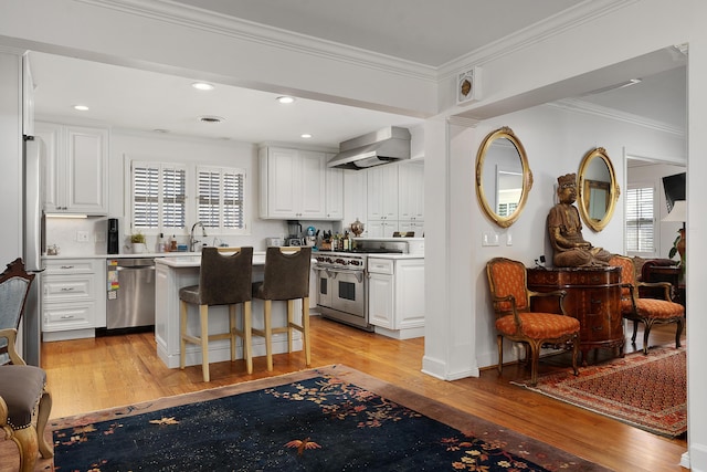 kitchen with white cabinetry, a kitchen breakfast bar, wall chimney exhaust hood, stainless steel appliances, and light hardwood / wood-style flooring