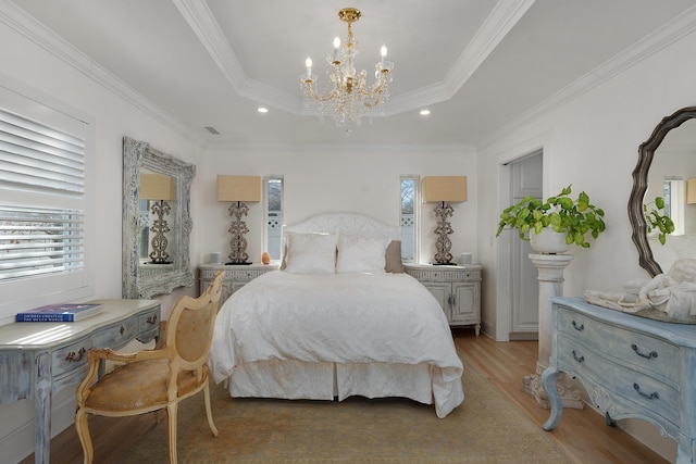 bedroom with crown molding, an inviting chandelier, light hardwood / wood-style floors, and a tray ceiling