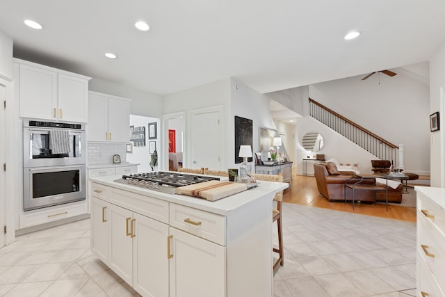 kitchen with a breakfast bar area, appliances with stainless steel finishes, white cabinetry, a kitchen island, and decorative backsplash