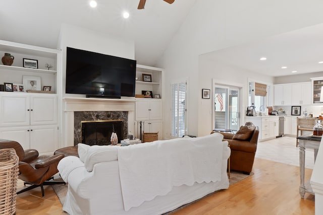 living room with ceiling fan, a fireplace, high vaulted ceiling, and light wood-type flooring