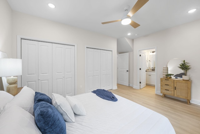 bedroom featuring ceiling fan, connected bathroom, light hardwood / wood-style flooring, and two closets