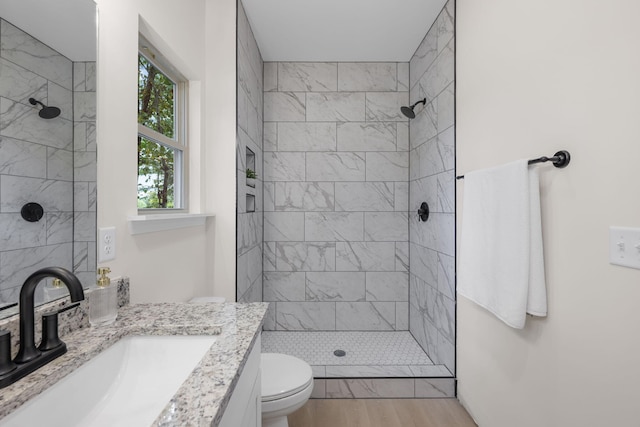 bathroom with hardwood / wood-style floors, tiled shower, toilet, and vanity