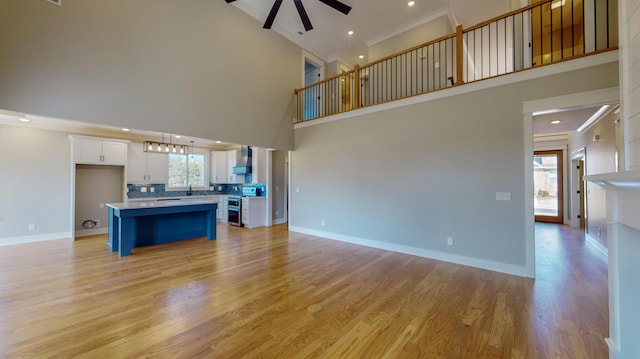 unfurnished living room with a high ceiling, ornamental molding, ceiling fan, and light hardwood / wood-style flooring