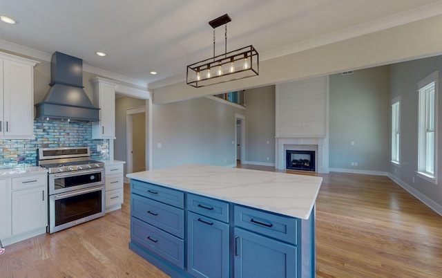 kitchen featuring premium range hood, decorative light fixtures, white cabinets, ornamental molding, and double oven range