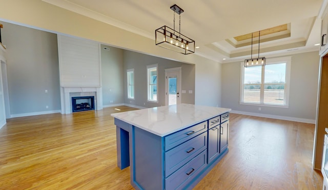 kitchen with hanging light fixtures, a tray ceiling, a large fireplace, and light wood-type flooring