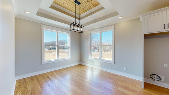 unfurnished dining area with a raised ceiling, an inviting chandelier, and light wood-type flooring