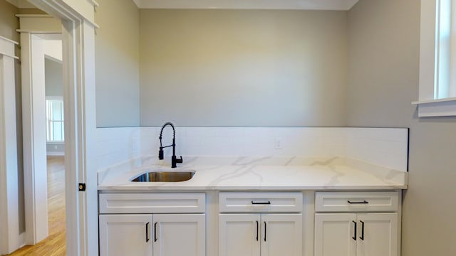 bar with light stone counters, light wood-type flooring, sink, and white cabinets