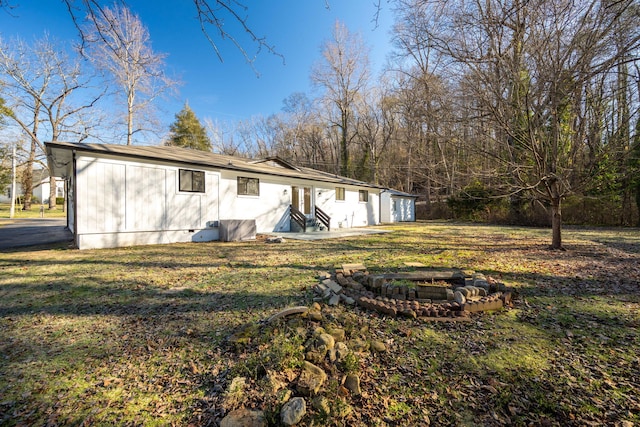 back of house with an outdoor fire pit and a lawn