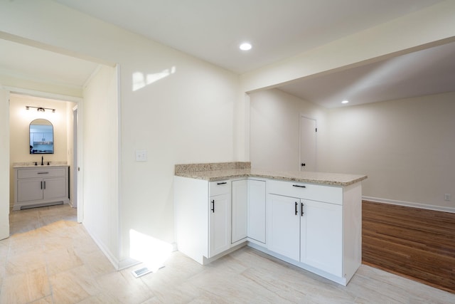 kitchen featuring white cabinetry, sink, light stone countertops, and kitchen peninsula