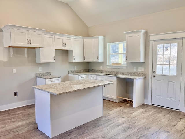 kitchen with light stone counters, a kitchen island, white cabinetry, light wood-type flooring, and lofted ceiling