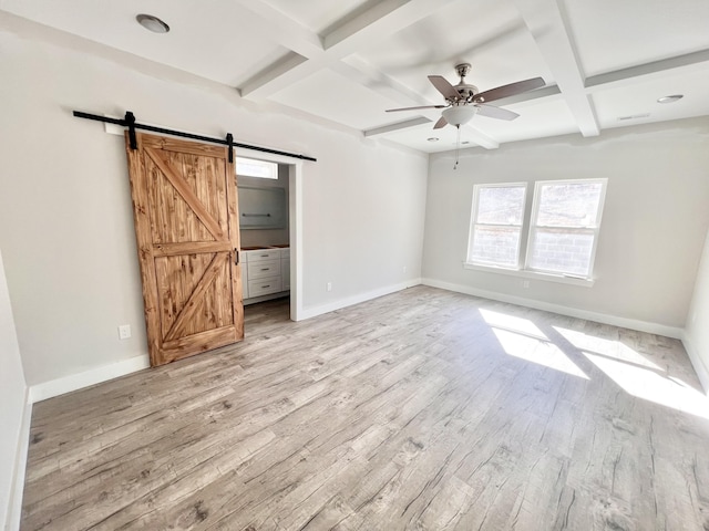 unfurnished bedroom featuring light wood-style flooring, a barn door, coffered ceiling, baseboards, and beam ceiling