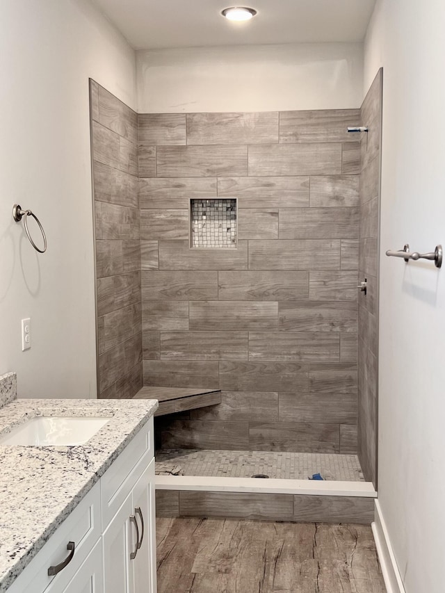 bathroom featuring a tile shower, wood finished floors, and vanity