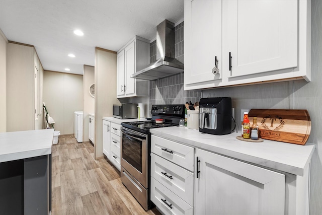 kitchen featuring stainless steel appliances, washer and dryer, white cabinets, and wall chimney exhaust hood