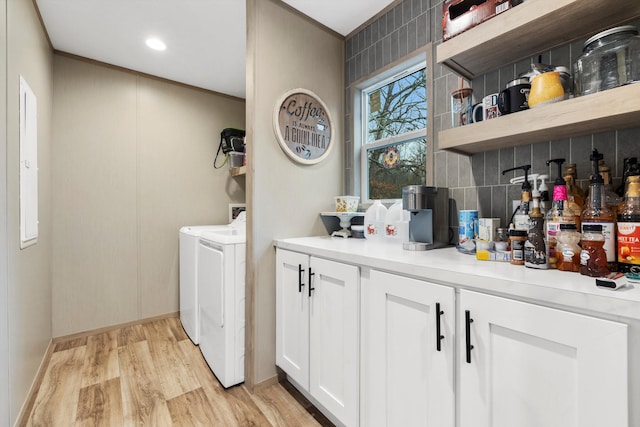 clothes washing area featuring separate washer and dryer, light hardwood / wood-style floors, and cabinets