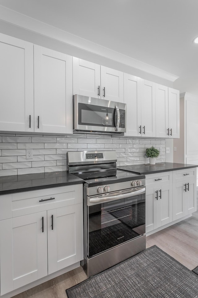 kitchen with hardwood / wood-style floors, decorative backsplash, stainless steel appliances, and white cabinets