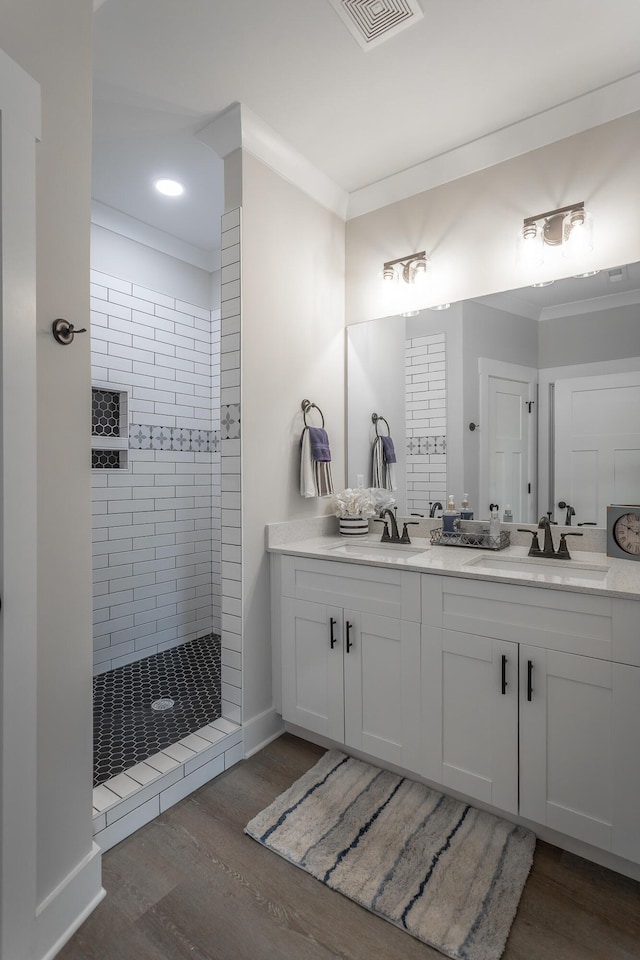 bathroom featuring hardwood / wood-style flooring, ornamental molding, vanity, and a tile shower