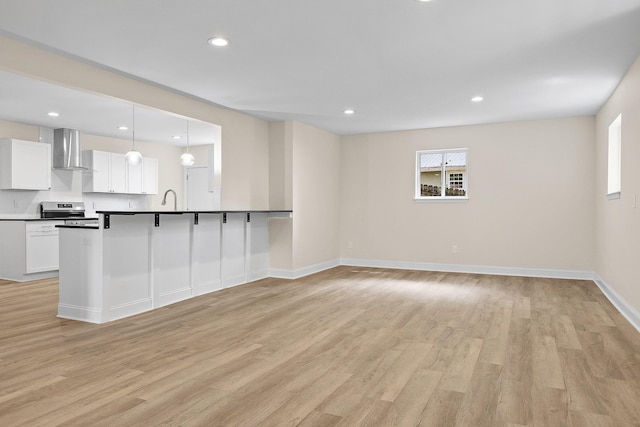 kitchen with light hardwood / wood-style flooring, white cabinets, stainless steel electric range oven, decorative light fixtures, and wall chimney exhaust hood