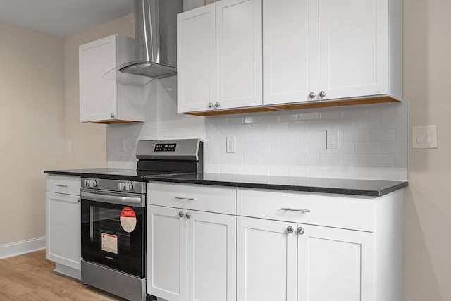 kitchen featuring electric stove, wall chimney exhaust hood, light hardwood / wood-style floors, and white cabinets