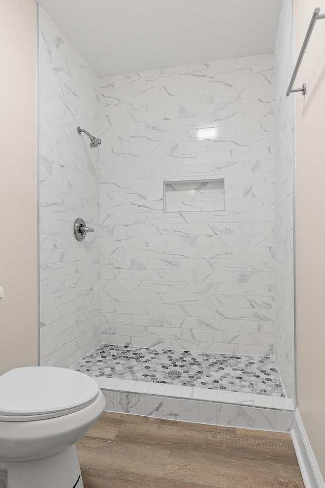 bathroom featuring hardwood / wood-style flooring, tiled shower, and toilet