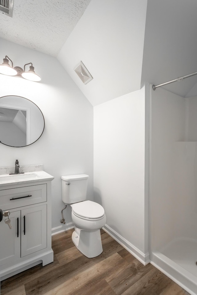 bathroom with vaulted ceiling, hardwood / wood-style flooring, vanity, toilet, and a textured ceiling