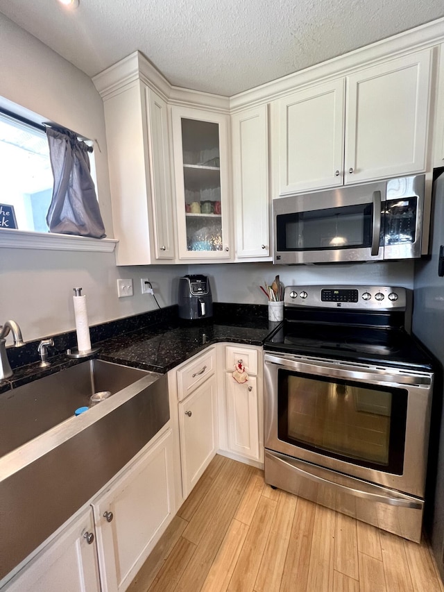 kitchen featuring sink, light hardwood / wood-style flooring, white cabinetry, dark stone countertops, and stainless steel appliances