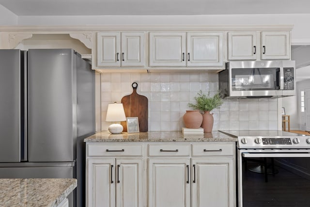 kitchen featuring light stone counters, cream cabinetry, stainless steel appliances, and backsplash