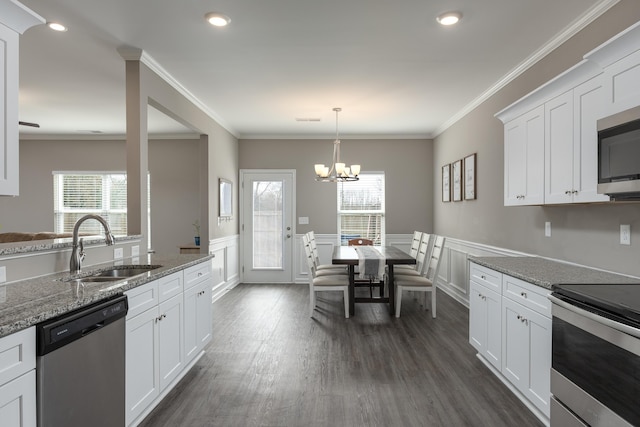 kitchen featuring a wainscoted wall, appliances with stainless steel finishes, dark wood-type flooring, ornamental molding, and a sink