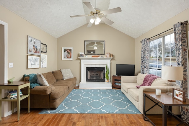 living room featuring a ceiling fan, a tile fireplace, a textured ceiling, wood finished floors, and vaulted ceiling