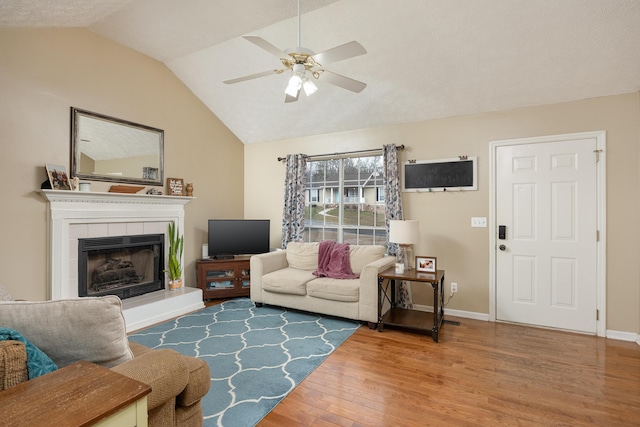 living room with wood finished floors, a ceiling fan, baseboards, lofted ceiling, and a tile fireplace