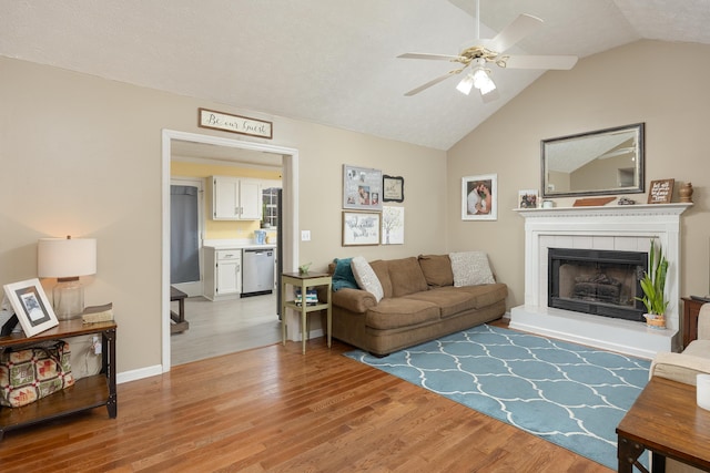 living area featuring light wood finished floors, baseboards, lofted ceiling, a tile fireplace, and a ceiling fan