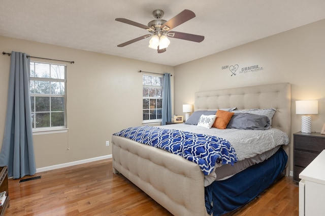 bedroom with a ceiling fan, light wood-style floors, visible vents, and baseboards