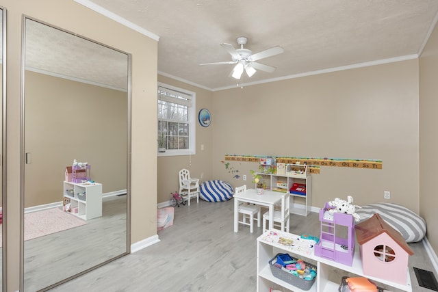 recreation room featuring baseboards, wood finished floors, a ceiling fan, and ornamental molding