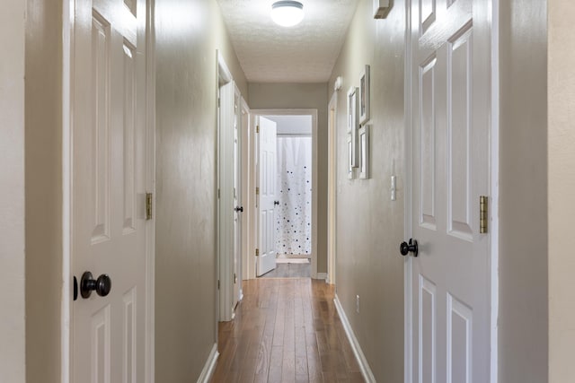 corridor featuring a textured ceiling, baseboards, and hardwood / wood-style flooring