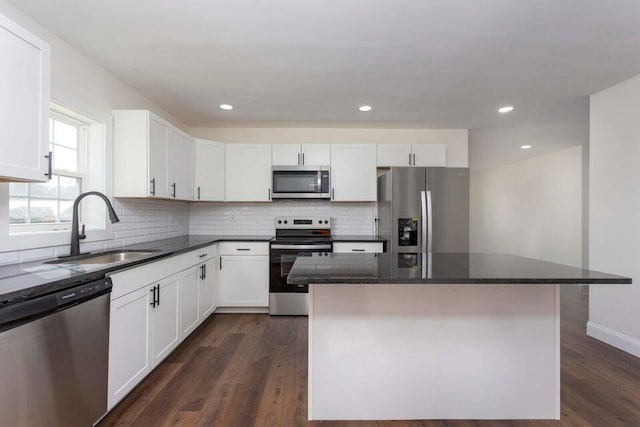 kitchen with appliances with stainless steel finishes, dark hardwood / wood-style floors, white cabinetry, sink, and a center island