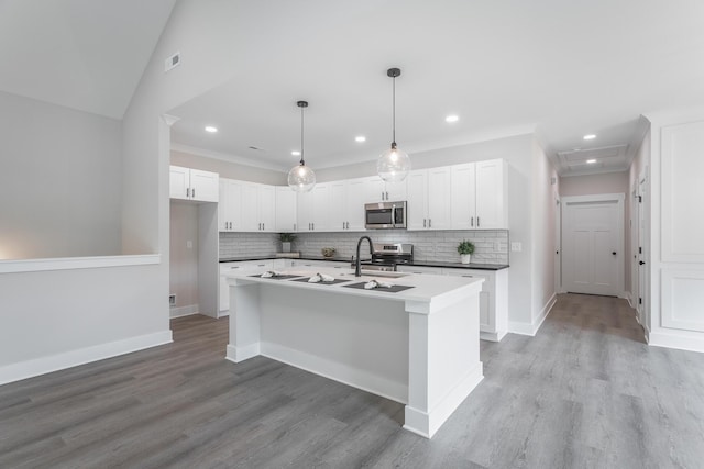 kitchen featuring vaulted ceiling, appliances with stainless steel finishes, decorative light fixtures, white cabinets, and a center island with sink