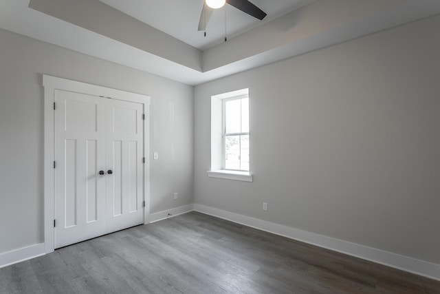 unfurnished bedroom featuring hardwood / wood-style flooring, a raised ceiling, ceiling fan, and a closet