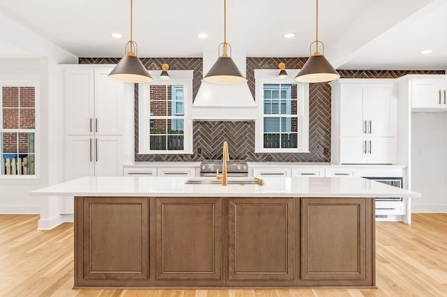 kitchen featuring pendant lighting, sink, a center island with sink, and white cabinets