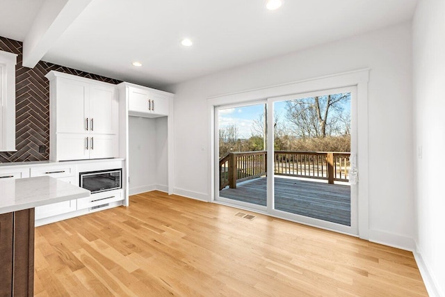 unfurnished living room with beamed ceiling and light hardwood / wood-style floors