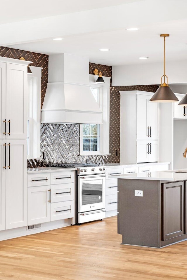 kitchen featuring tasteful backsplash, decorative light fixtures, custom range hood, light hardwood / wood-style floors, and white cabinets